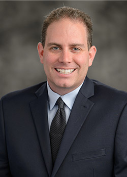 Andrew Schwarz headshot wearing a dark suit with grey tie. 